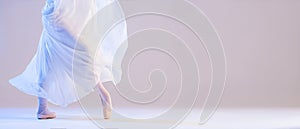 The legs of a ballerina in pointe shoes stand under a developing flying skirt on a white background