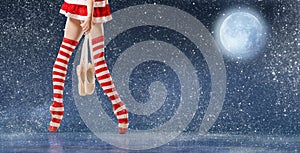 Legs of a ballerina on pointe shoes in striped golfs of Santa Claus walks against the backdrop of a night snowy sky and the moon photo