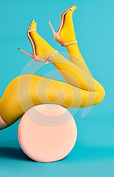 Legs of beautiful young woman wearing bright yellow tights and high heels shoes lying on pouf