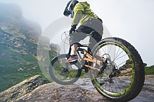 Legs of bicyclist and rear wheel close-up view of back mtb bike in mountains against background of rocks in foggy
