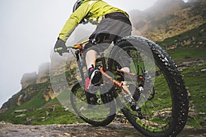 Legs of bicyclist and rear wheel close-up view of back mtb bike in mountains against background of rocks in foggy