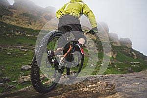 Legs of bicyclist and rear wheel close-up view of back mtb bike in mountains against background of rocks in foggy