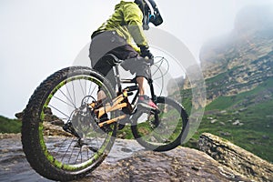 Legs of bicyclist and rear wheel close-up view of back mtb bike in mountains against background of rocks in foggy