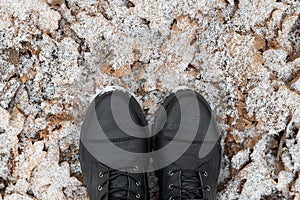 Legs in black boots on snow-covered leaves.