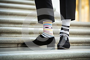 Legs with black pants, different pair of socks and black shoes standing on stairs outdoors. Young man foots in
