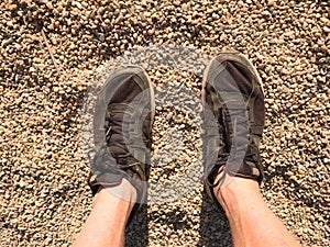 Legs in black sport shoes walking on sandy ground. Man hairy skin legs in black shoes