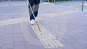 Legs of blind person searching special tactile tiles using cane. Blind man walking with a cane in the street
