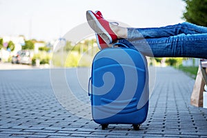 Legs in blue jeans and red sneakers on a blue suitcase