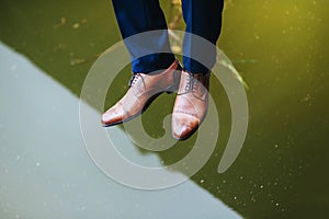 Legs and boots of a young man over the lake with reflection