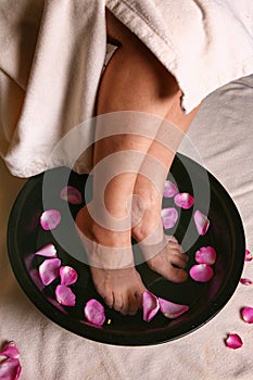 Legs in a bowl of water with flower petals. SPA