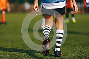 Legs of boy footballer in boots football cleats. Player walking on green grass soccer field at the stadium