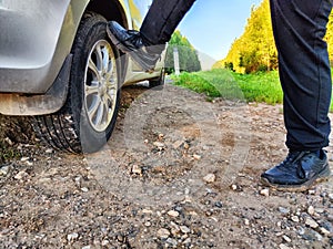 The legs of a boy kicking a car wheel on roadside. Vandal, hooligan, thug. Summer car journey