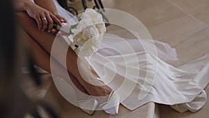 Legs of the bride in a dress with a bouquet. The bride is sitting on the steps.