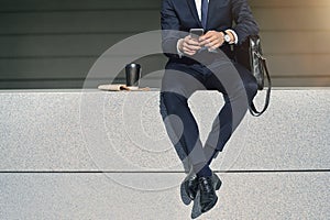 Legs of businessman searching information in smartphone