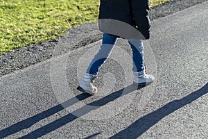 Legs of a child in jeans and sneakers on the road