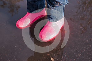 Legs of child in rainboots standing in puddle.Kids in fall. close-up of a baby girls legs with pink rubber boots during