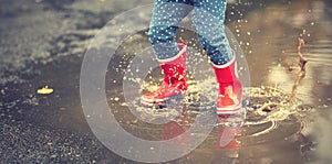 Legs of child in red rubber boots jumping in autumn puddles photo