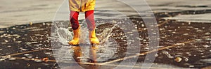 Legs of child with rubber boots jump in puddle on autumn walk