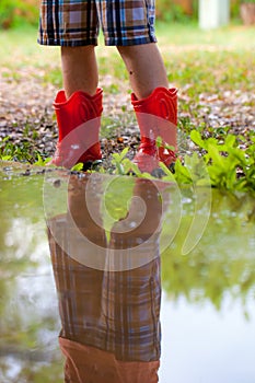 Legs of child wearing pair of red rubber boots with reflection i