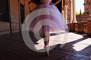 Legs of a classical ballet dancer in which she is standing on tiptoe with her hands on her hips. Classical ballet