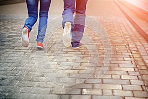 Legs close-up of a loving couple running along a sidewalk tile, romance, love, blue jeans, sneakers. Concept idyll