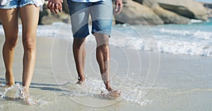 Legs, couple and holding hands at the beach while walking, bond and enjoy water splash, freedom or travel. Love, walk