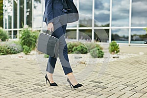 Legs detail of business woman on the way to office, walking outdoors holding a laptop case, wearing business suit and