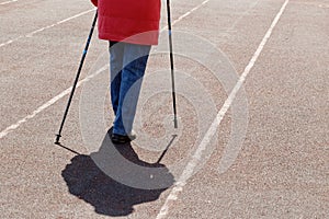 Legs of an elderly woman practicing Nordic walking on a sports field. Self-isolation during the NCOV-19 Coronavirus pandemic.