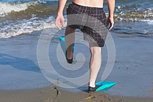 Legs of fat man in the swimming flippers on the sand on the beach