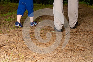 The legs of a father and a son against the background of nature. Dad and child walk forward in the woods. Family walk, Father`s