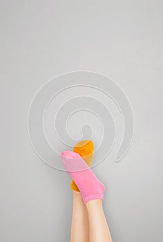 Legs and feet with cute sock. Woman wearing pastel pink and yellow socks raised crossed leg  on gray background. Top view