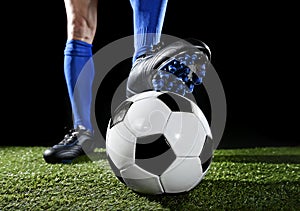 Legs and feet of football player in blue socks and black shoes posing with the ball playing on green grass