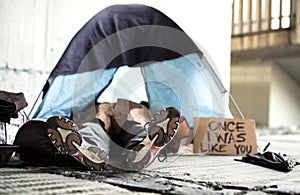 Legs and feet of homeless beggar man lying on the ground in city, sleeping in tent.