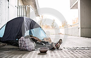 Legs and feet of homeless beggar man lying on the ground in city, sleeping in tent.