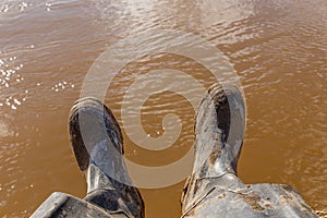 Legs of a fisherman sitting in dirty rubber boots
