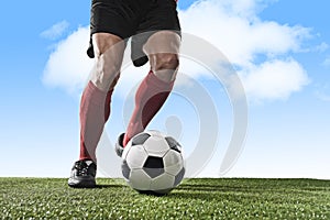 Legs of football player in red socks and black shoes running and dribbling with ball playing outdoors