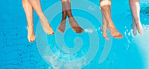 Legs of four friends common people different race sitting by the swimming pool in sunny day.