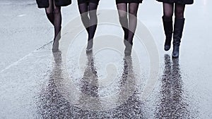 Legs of four woman in shoe on heels walk in lockstep on wet asphalt. Slow motion