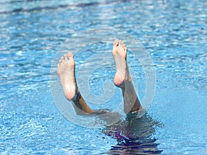 Legs of a girl diving into the water, sticking out of the pool