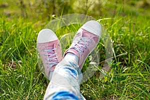 Legs of the girl in jeans and white and pink on the green grass in the summer