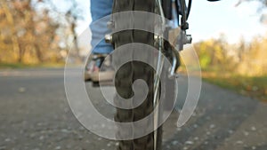 Legs of girl pushing bicycle pedals. Wheel with tread rides, close-up. Bike rides on asphalt road.