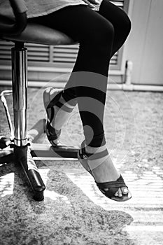 Legs of the girl in sandals sitting in a chair. black and white photo. girl in sandals