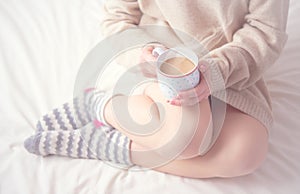 Legs of girl warm woolen socks and cup of coffee warming, winter morning in bed