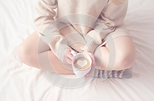 Legs of girl warm woolen socks and cup of coffee warming, winter morning in bed