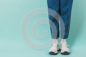 Legs of a girl in white socks, white sneakers and jeans on a blue background. Place for text