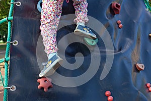 The legs of a girl who stand on hooks on a slide. children& x27;s climbing wall in the park