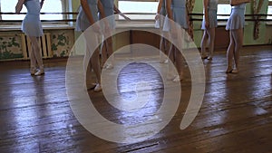 Legs of girls standing in third position during ballet lesson in frayed classroom.