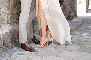 Legs of the groom and the bride embracing near the stone wall on the narrow street of the old gorol, close-up