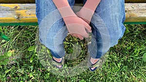 Legs and hands of a lonely sad boy sitting outdoors on a bench, unhappy depressed child with discrimination and bullying