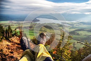 Legs of hiker with hiking boots on top of the hill with beautiful landscape under